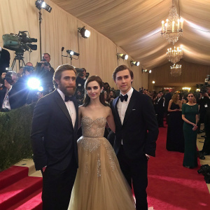 Jake Gyllenhaal, Lily Collins, and Paul Dano at a gala event. Lavish setting with red carpet, photographers flashing cameras, and an array of attendees in formal wear.