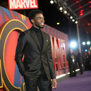 Chadwick Boseman, dressed in a sleek black suit, attends the Hollywood premiere for a Marvel film. Vibrant backdrop featuring bold Marvel logos