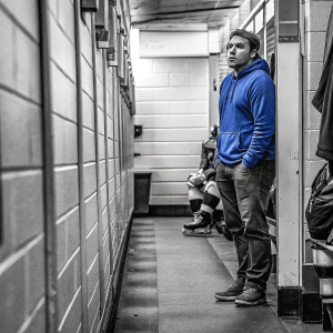 Bo Horvat, Vancouver Canucks player, standing in locker room. Wearing casual attire, blue team hoodie. Colleagues in background