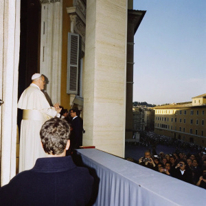 Pope Francis addressing the crowd from the Vatican balcony. Surrounded by believers and media. Bright sunny day in the Eternal City.