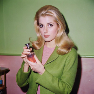 young Catherine Deneuve from the film Belle De Jour with a bottle of perfume in hand