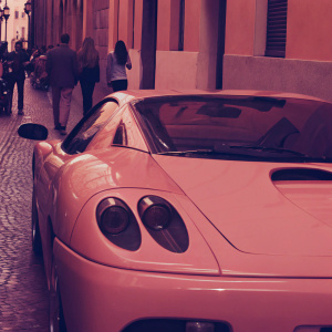 Pink Ferrari Modena F360 Spider Sbarro GT8 parked in a bustling city street. The car's sleek design stands out against a backdrop of people and buildings.