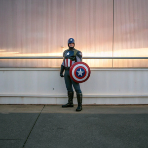 Steve Rogers, dressed as Captain America, poses against a white backdrop at a comic-con event.