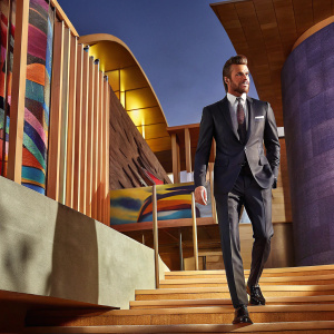 David Beckham in a sleek black suit and tie, posing for a fashion shoot. Surrounded by futuristic architecture and vibrant murals.