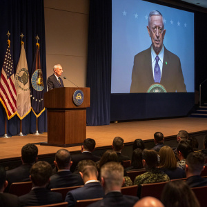 James Mattis delivers keynote speech at Pentagon conference. Large projection screen behind him features his image.