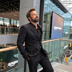 Ben Affleck, bearded actor, in a sleek black suit, posing at Amazon headquarters unveiling event.