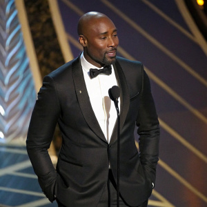 Morris Chestnut in a sleek black tuxedo, without hair, standing solo at an awards ceremony.