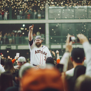 Brian McCann, in a Houston Astros jersey, celebrates victory with fans at a stadium. Crowd cheering, including mascot and Astros-themed attire