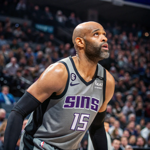 Vince Carter, bald with beard, in action at a packed arena. Wearing gray and black Sacramento Kings jersey. Number 15 clearly visible. Focused gaze.