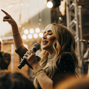 Sabrina Carpenter at Build Series. Holding microphone, speaking passionately. Sparkling jewelry, joyous expression.