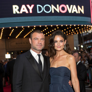 Liev Schreiber and Katie Holmes at the premiere of 'Ray Donovan'. Formal attire, standing in front of crowded theater. Event logos on screen.