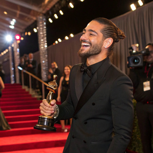 Maluma, Colombian singer, accepting award. Red carpet event. Wearing black suit, smiling.
