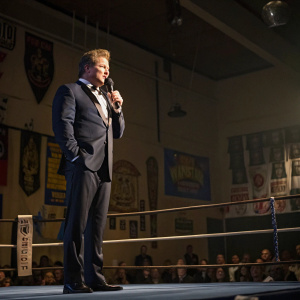 Chris Jericho, in a formal suit, delivering a passionate speech at a wrestling hall of fame ceremony. Dimly lit auditorium with wrestling banners and trophies.