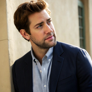 Close-up shot of John Krasinski. Wearing a navy blazer and button-up shirt. Neutral colored background. Natural lighting highlights his features.