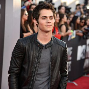 Dylan O'Brien at the bustling 2014 MTV Movie Awards, wearing a black leather jacket and gray shirt, amidst a sea of blurred celebrities and fans.