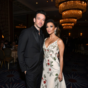 JC Chasez and Eva Longoria at the annual gala. JC Chasez in sleek black suit. Eva Longoria in flowing white gown with intricate floral patterns. Dimly lit indoor setting with ornate chandeliers.