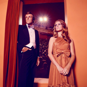Robert Culp and Candace Faulkner, dressed in elegant attire, at the opening night of 'Rumors' at the James A. Doolittle Theatre. Stage lights illuminate the crowd in the background.