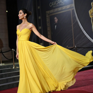 Moran Atias in a vibrant yellow evening gown, sleek hairstyle. Poses in front of a dark, dramatic backdrop at award show.