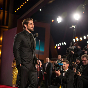 Aaron Rodgers, in a sleek black suit, receiving an award at a Hollywood gala. Flashy lights and paparazzi in the background.