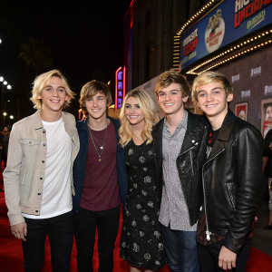 R5 band members Ross Lynch, Riker Lynch, Rydel Lynch, Ellington Ratliff, and Rocky Lynch posing together at the premiere of Big Hero 6 at El Capitan Theatre. They wear casual outfits and smile for the camera.