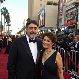 Alfred Molina and Jill Gascoine at a Hollywood premiere. Wearing tuxedo and evening gown respectively. Crowded, red carpet setting.