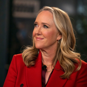 Jennifer Salke, Amazon Studios executive, blonde hair, red blazer, soft smile. Close-up shot with blurred dark background.