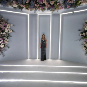 Rosie Huntington-Whiteley at the Revolve Awards, donning a shimmering black dress. Festive floral backdrop.