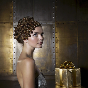 Photogenic ad campaign for Sisel Kaffe featuring a model with a unique hairstyle made from coffee beans. Rich brown and gold colors dominate the luxurious imagery, encouraging Valentine's Day gifts with a premium touch.