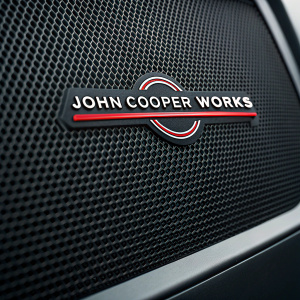 John Cooper Works logo for Mini Cooper, sleek speaker design. Dark background with mesh-like surface.