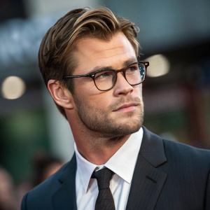 Close-up portrait of Chris Hemsworth. Wears dark suit, tie, and glasses. Expression is serious and intense.