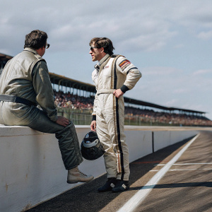 Carl Edwards, wearing NASCAR racing gear, chats with another driver. Crowd and track visible in the background.