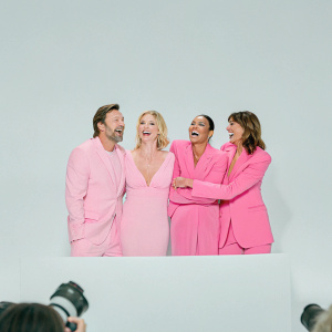 Hugh Jackman, Rebecca Romijn, Halle Berry, and Famke Janssen laughing and smiling at a press conference. Event venue with bright lights and cameras