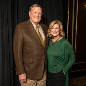 Ken Howard and Linda Fetters, smiling and posing at a charity gala. Ken in a brown suit, Linda in a green top. Dark, elegant backdrop
