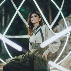 Zendaya, dressed in futuristic outfit, posing in a studio. Neon lights create an abstract background.