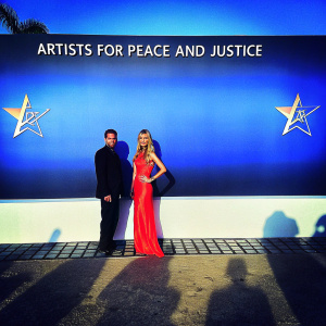 Petra Nemcova and Jamie Belman at the Hollywood Domino Gala, benefiting Artists For Peace And Justice. Petra in a stunning red, strapless, sleeveless gown. The background features bold logos and text on a black backdrop.