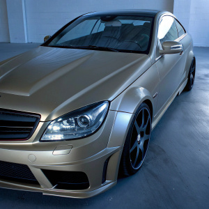 A stunning golden Mercedes-Benz C63 AMG parked in an indoor garage. The car's sleek design and rich metallic finish shine under diffused lighting.