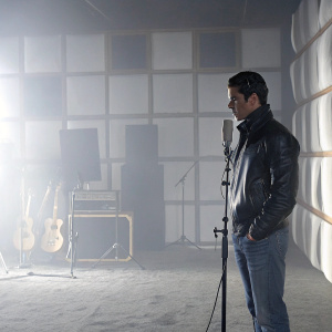 Cristiano Ronaldo, wearing a black leather jacket and jeans, is in a dimly lit recording studio. The background shows various musical instruments and soundproof walls.