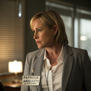 Patricia Arquette in a dimly lit office, portraying Allison Dubois. Wears gray blazer, white shirt, and name badge.
