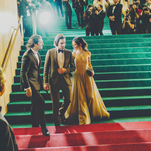 Dacre Montgomery, Natalia Dyer, and Joe Keery at the Met Gala. Dapper suits and elegant gowns. Crowded red carpet, flash photography.