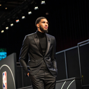 Jayson Tatum, wearing a sleek, black suit, standing confidently at a press conference. Dark, sleek stage background.