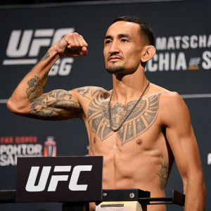 Max Holloway, MMA fighter, at UFC weigh-in. Determined look. Tattoos visible. UFC branding in background.
